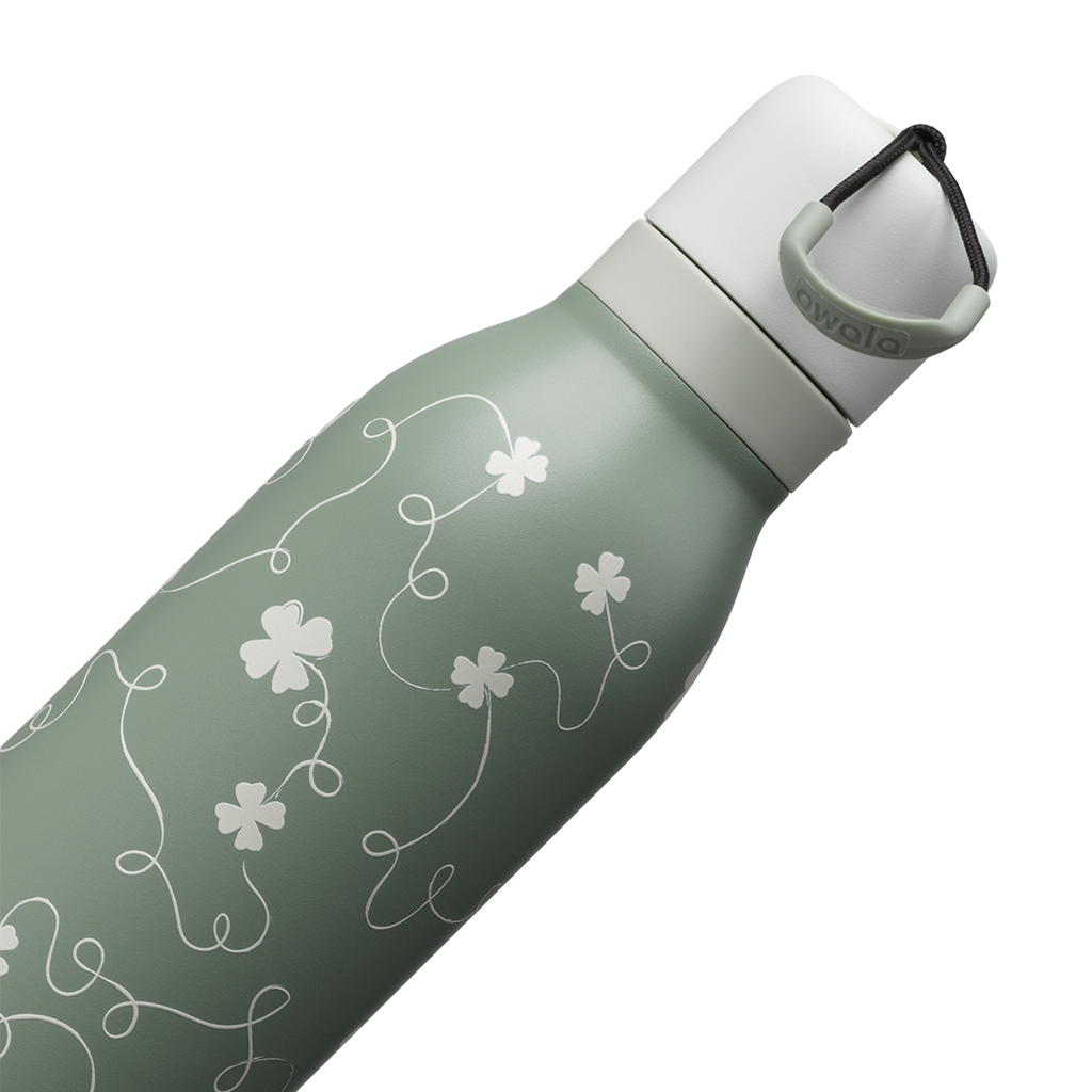 Owala FreeSip Twist 24oz in Clover Achiever, close-up of the sage green body with white clover and vine pattern and the white twist cap with sage carry string and dark carry string grip